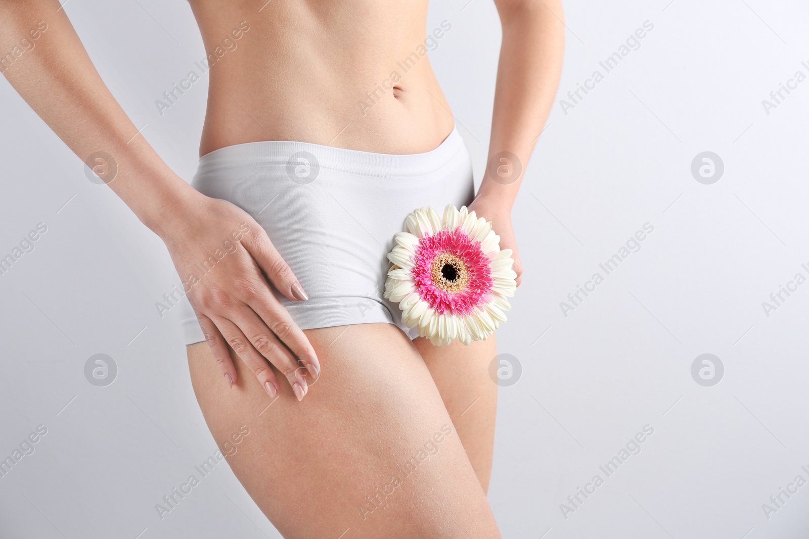Photo of Young woman holding flower near underwear on white background. Gynecology