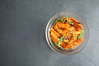 Photo of Glass bowl with baked sweet potato slices and arugula on grey background, top view. Space for text