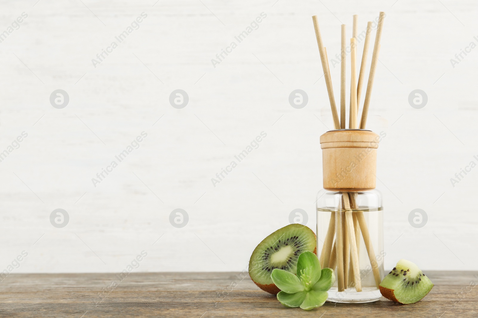 Photo of Aromatic reed freshener and kiwi on wooden table against light background. Space for text