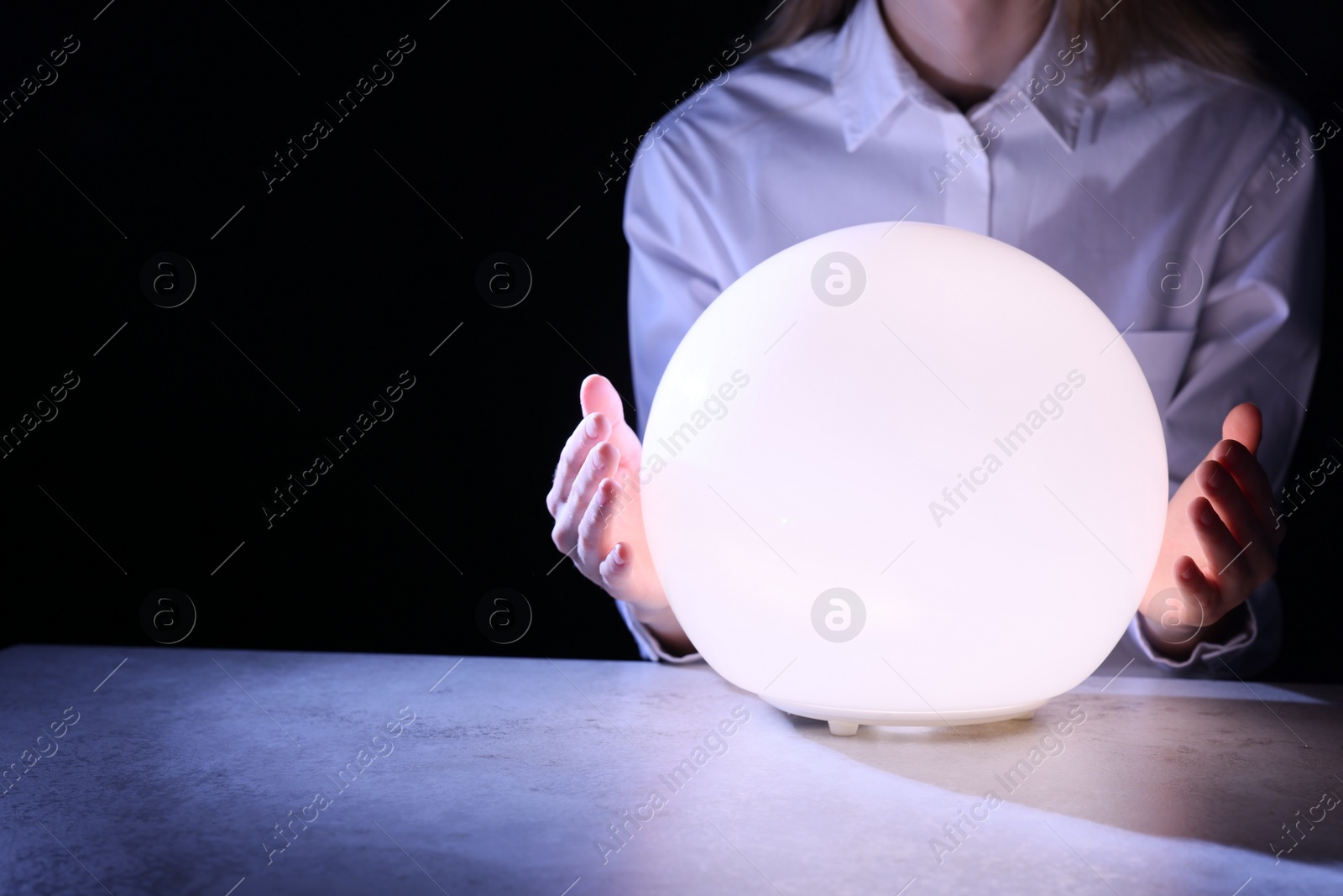 Photo of Businesswoman using glowing crystal ball to predict future at table in darkness, closeup. Space for text