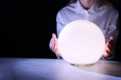 Businesswoman using glowing crystal ball to predict future at table in darkness, closeup. Space for text