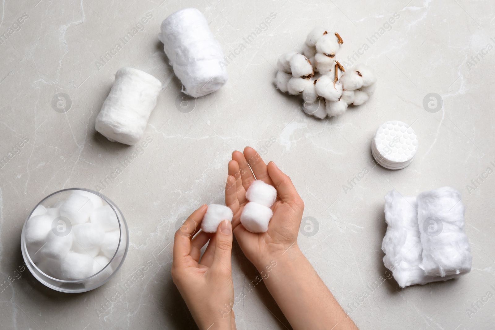 Photo of Woman holding fluffy cotton balls over gray table, top view