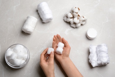 Woman holding fluffy cotton balls over gray table, top view