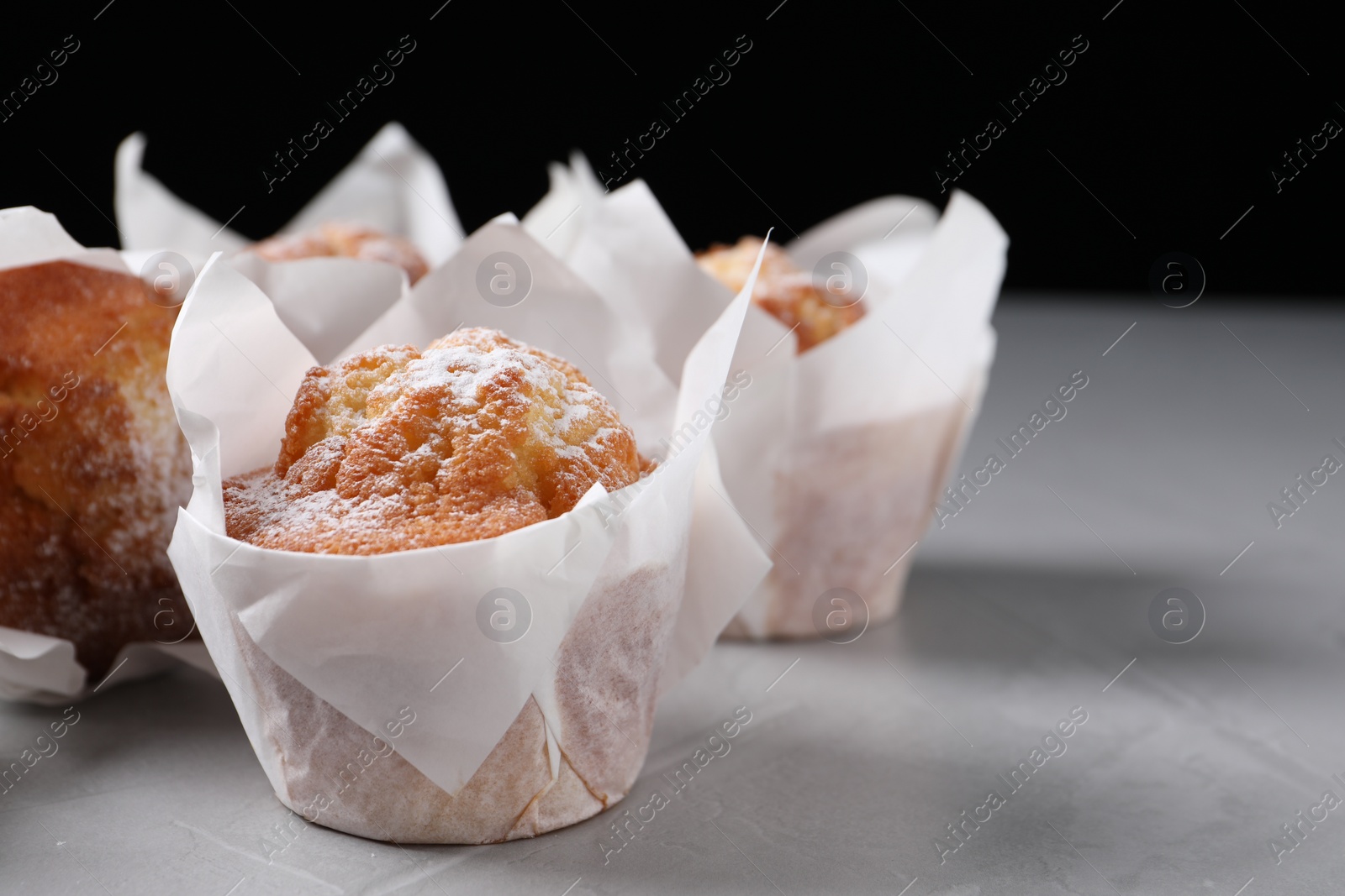 Photo of Delicious muffins with powdered sugar on grey table, closeup