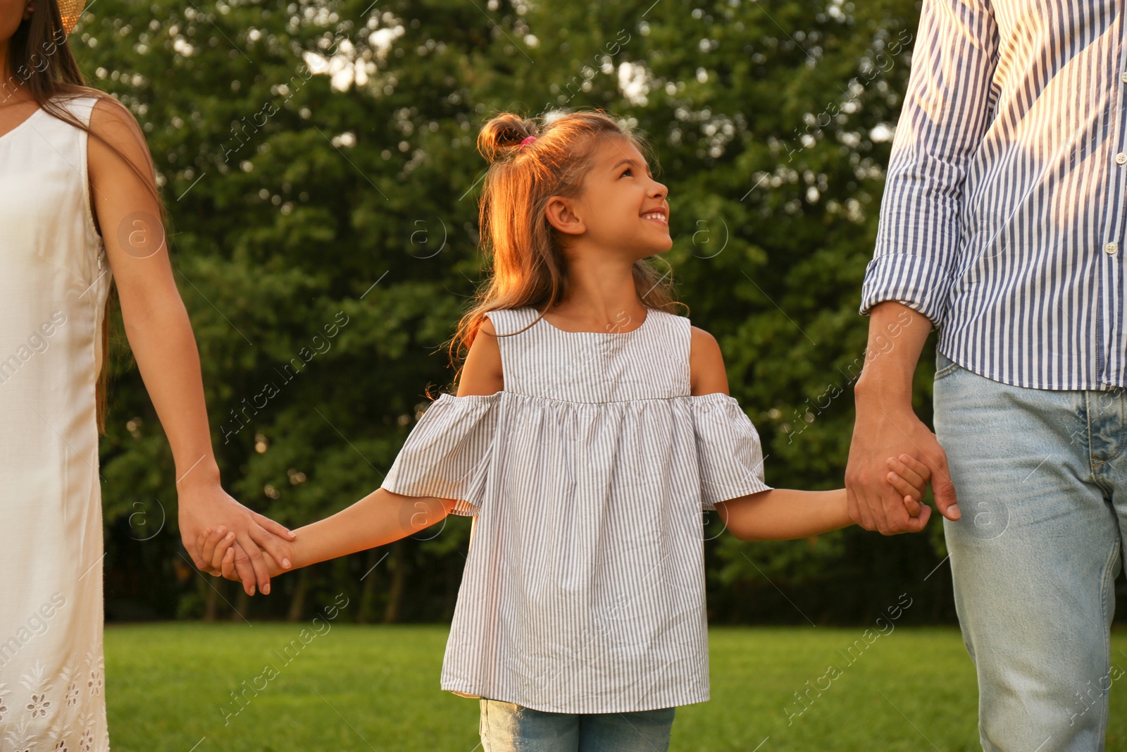 Photo of Little girl and her parents holding hands in park. Happy family