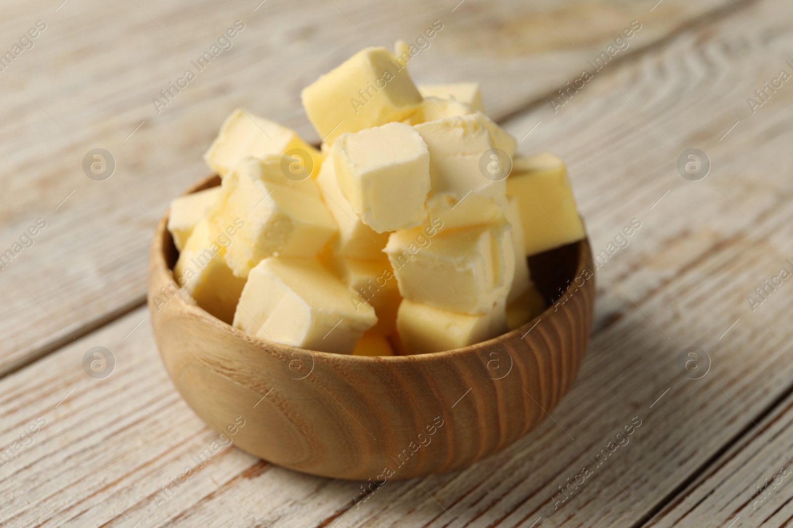 Photo of Tasty butter cubes in bowl on light wooden table