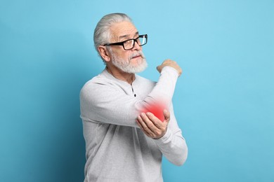 Image of Senior man suffering from pain in elbow on light blue background