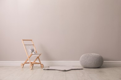 Toy stroller with bear and pouf near grey wall in child room. Interior design