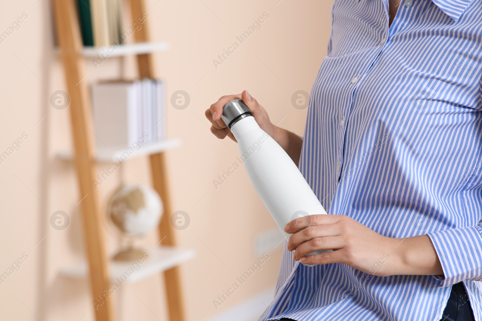 Photo of Woman holding thermo bottle indoors, closeup. Space for text