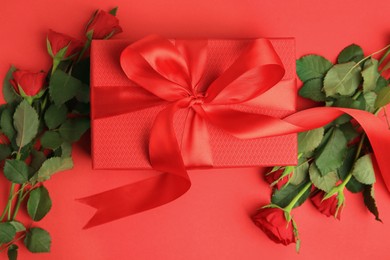 Photo of Beautiful gift box with bow and roses on red background, flat lay