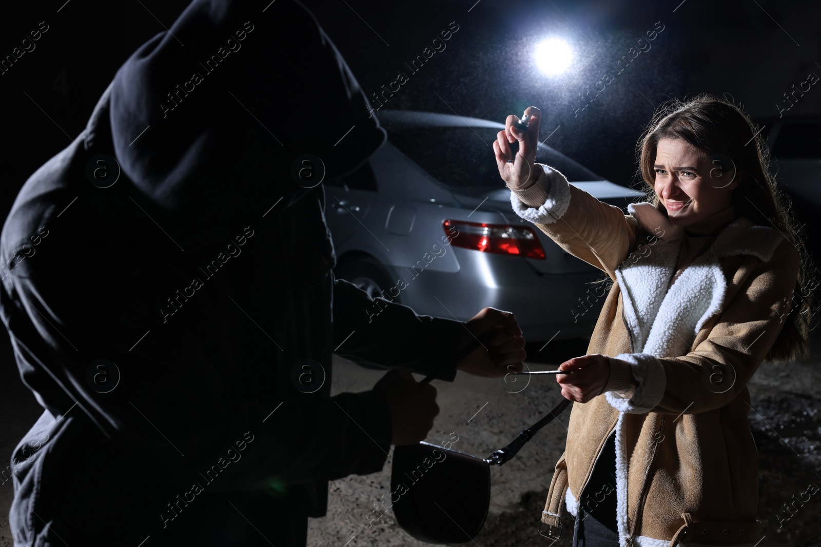 Photo of Woman using pepper spray while thief trying to steal her bag outdoors at night. Self defense concept