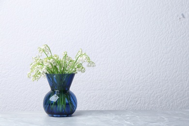 Beautiful lily of the valley bouquet in vase on table near white wall, space for text