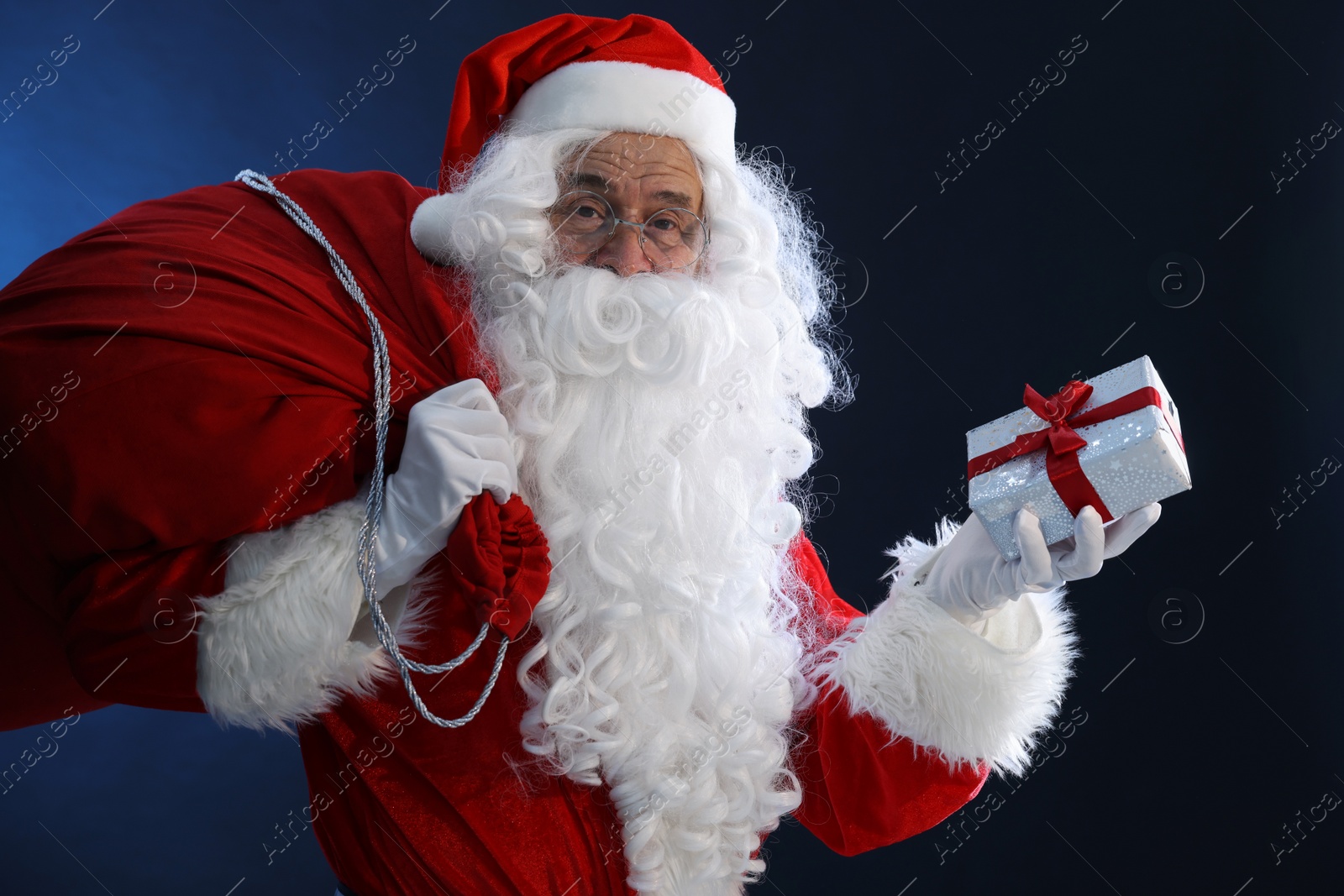 Photo of Santa Claus with Christmas gift and bag on dark blue background