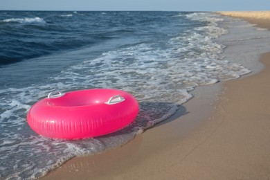 Bright pink inflatable ring on sandy beach near sea, space for text