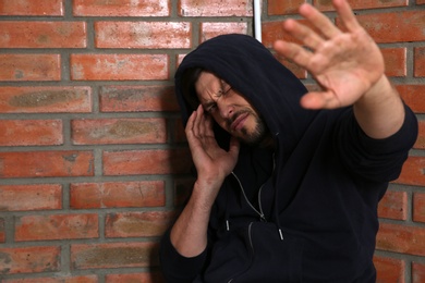 Young addicted man sitting near brick wall after using drugs