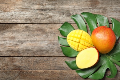 Photo of Flat lay composition with ripe mangoes, monstera leaf and space for text on wooden background