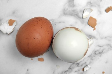 Photo of Boiled eggs and pieces of shell on white marble table, flat lay