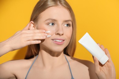 Photo of Beautiful young woman applying sun protection cream onto her face against orange background