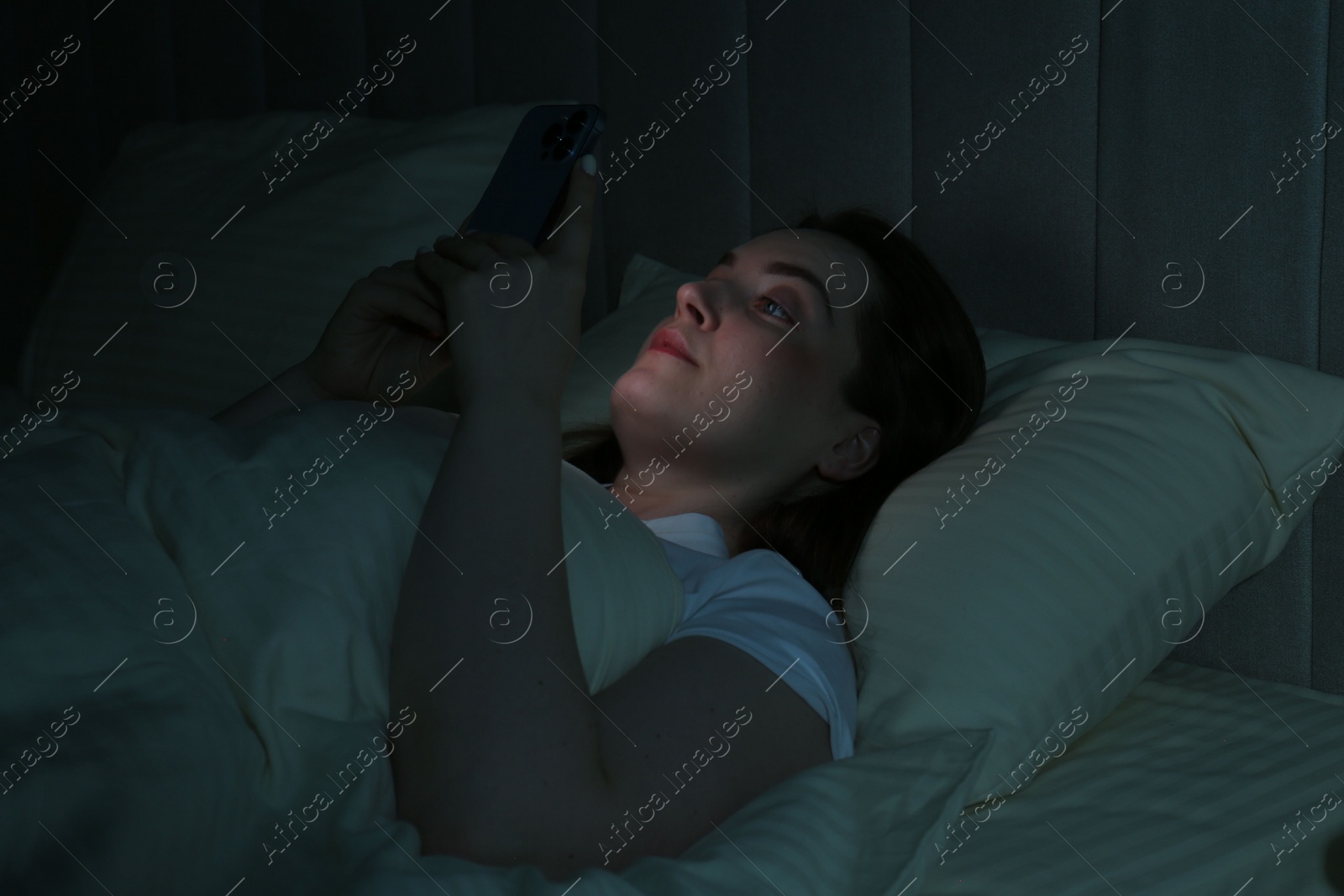 Photo of Woman using smartphone on bed at night. Internet addiction