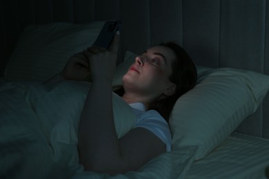 Photo of Woman using smartphone on bed at night. Internet addiction