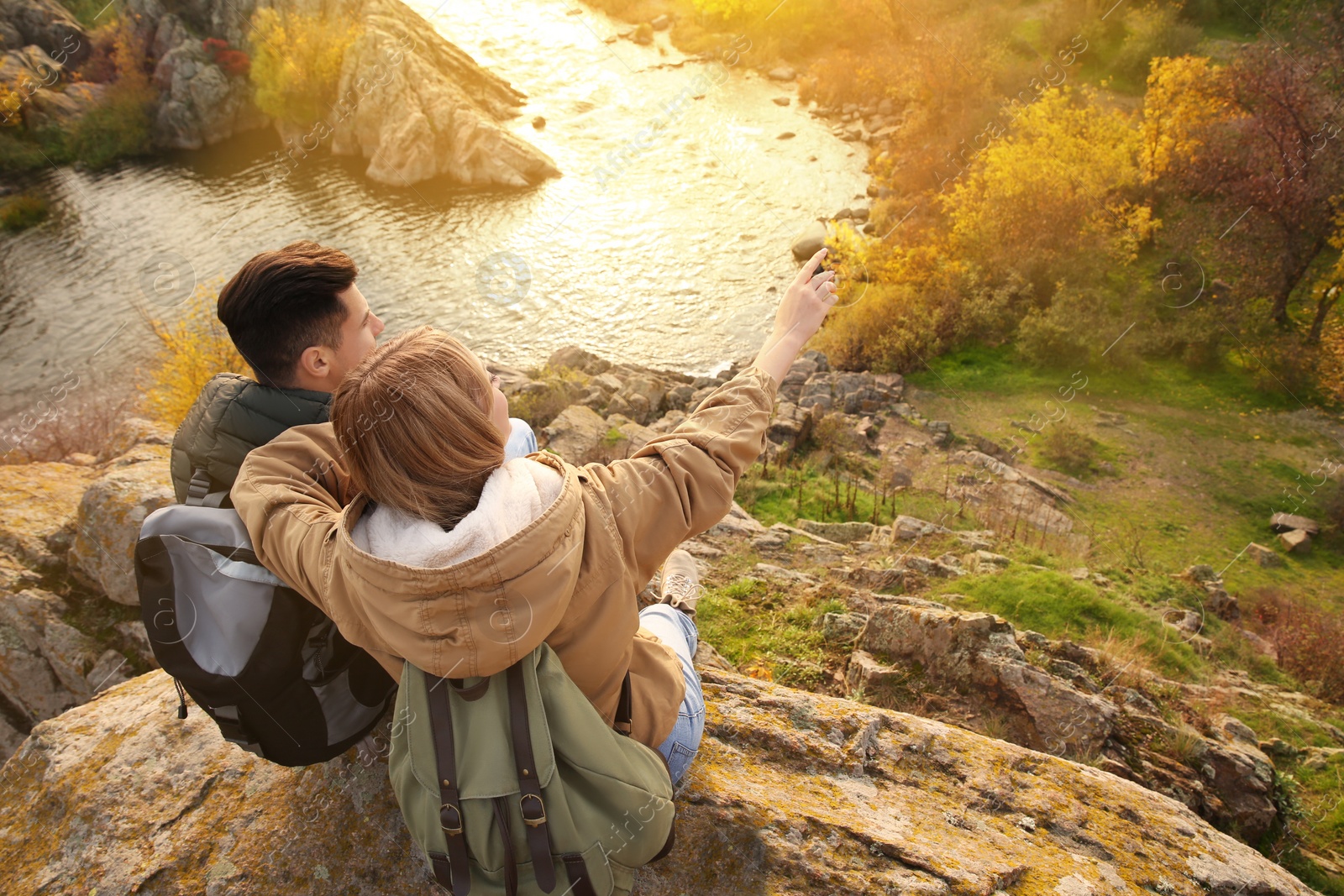 Photo of Couple of hikers with travel backpacks sitting on steep cliff