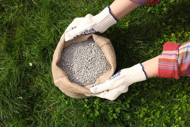 Photo of Woman with bag of fertilizer on green grass outdoors, top view