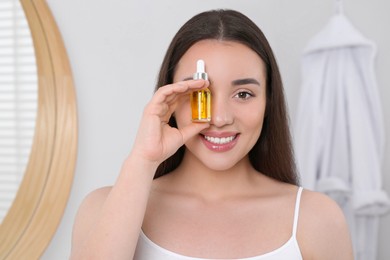 Happy young woman with bottle of essential oil in bathroom