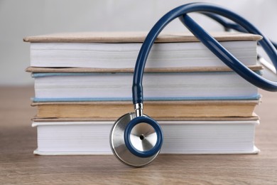 Photo of Stack of student textbooks and stethoscope on wooden table, closeup. Medical education