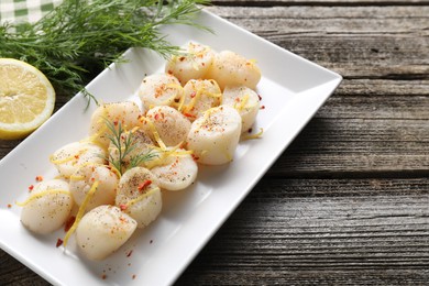 Photo of Raw scallops with spices, dill and lemon zest on wooden table, closeup. Space for text