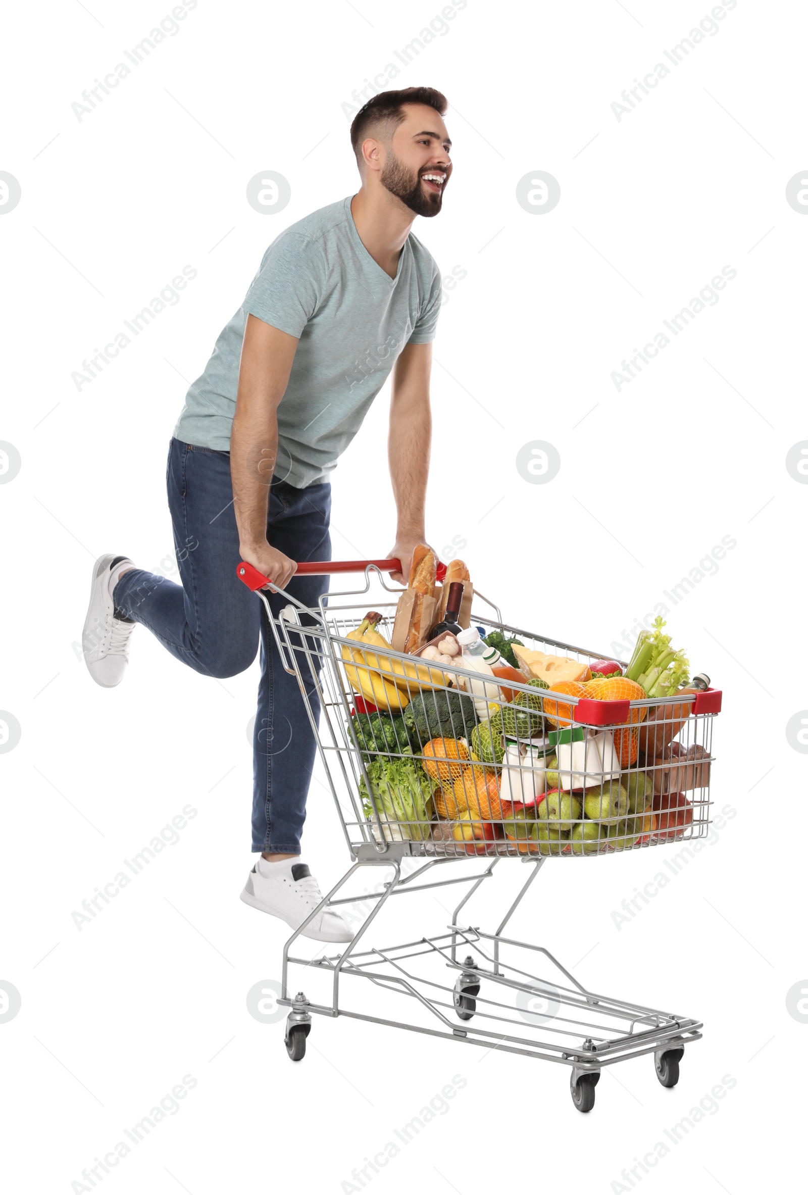 Photo of Happy man with shopping cart full of groceries on white background