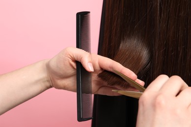 Hairdresser cutting client's hair with scissors on pink background, closeup