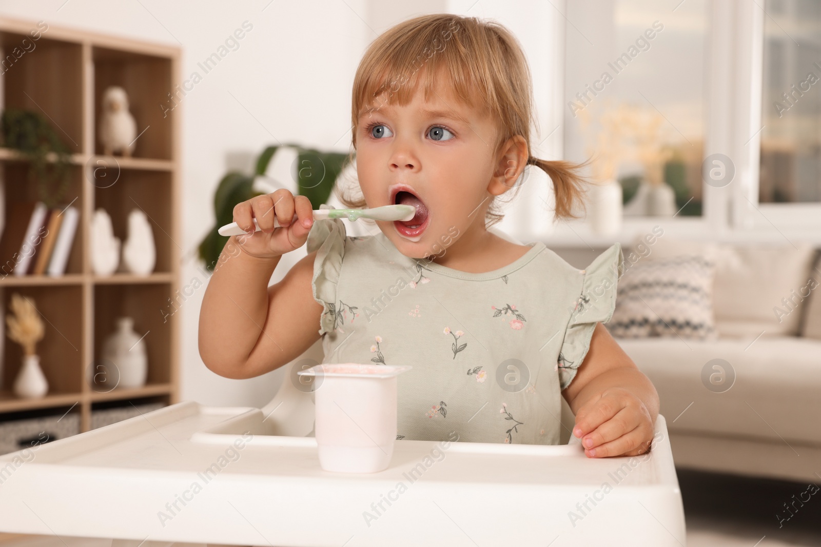 Photo of Cute little child eating tasty yogurt with spoon at home