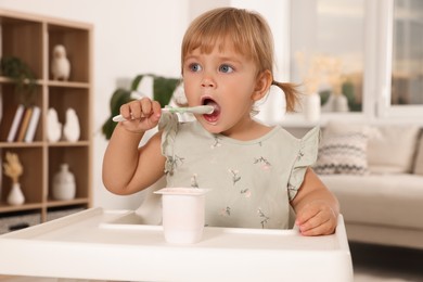 Photo of Cute little child eating tasty yogurt with spoon at home