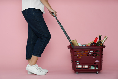 Woman with shopping basket full of different products on pink background, closeup