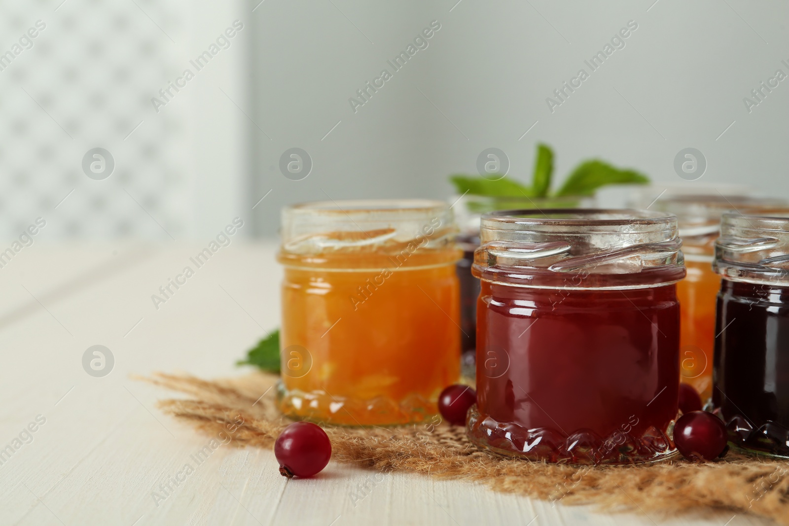 Photo of Jars of different jams on white table, space for text