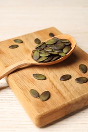 Photo of Spoon with pumpkin seeds on wooden table, closeup