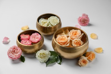 Photo of Tibetan singing bowls with water and different beautiful rose flowers on white background
