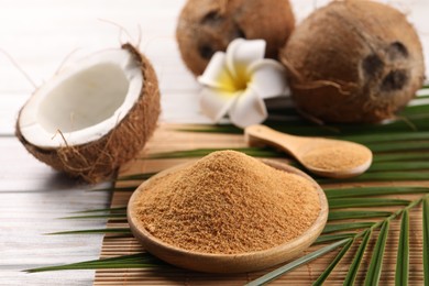 Photo of Coconut sugar, palm leaves, fruits and bamboo mat on wooden rustic table, closeup