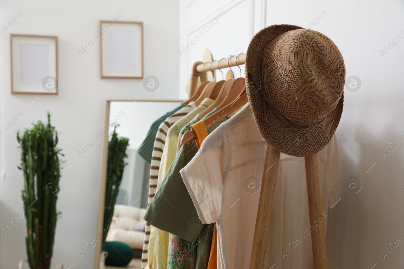 Photo of Rack with hanging clothes and straw hat indoors. Interior design