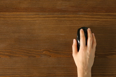 Woman using computer mouse on wooden background, top view. Space for text