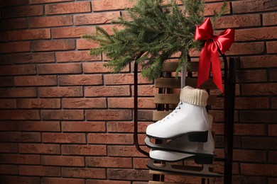 Sleigh with pair of ice skates and fir branches near brick wall, space for text
