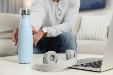 Photo of Man taking thermo bottle from white table at home, closeup