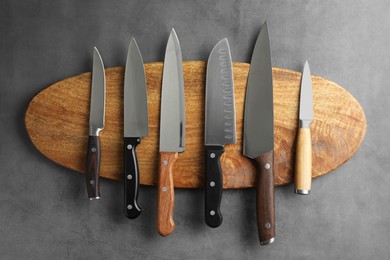 Photo of Many different knives and wooden board on grey textured table, flat lay
