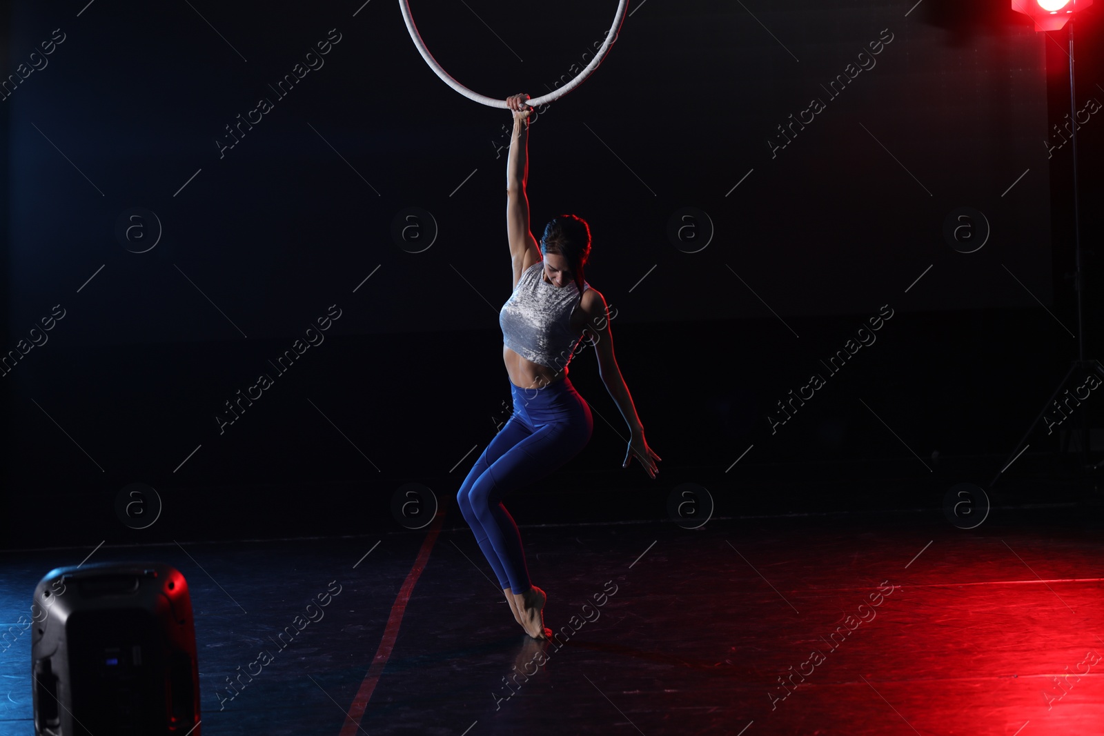 Photo of Young woman performing acrobatic element on aerial ring indoors