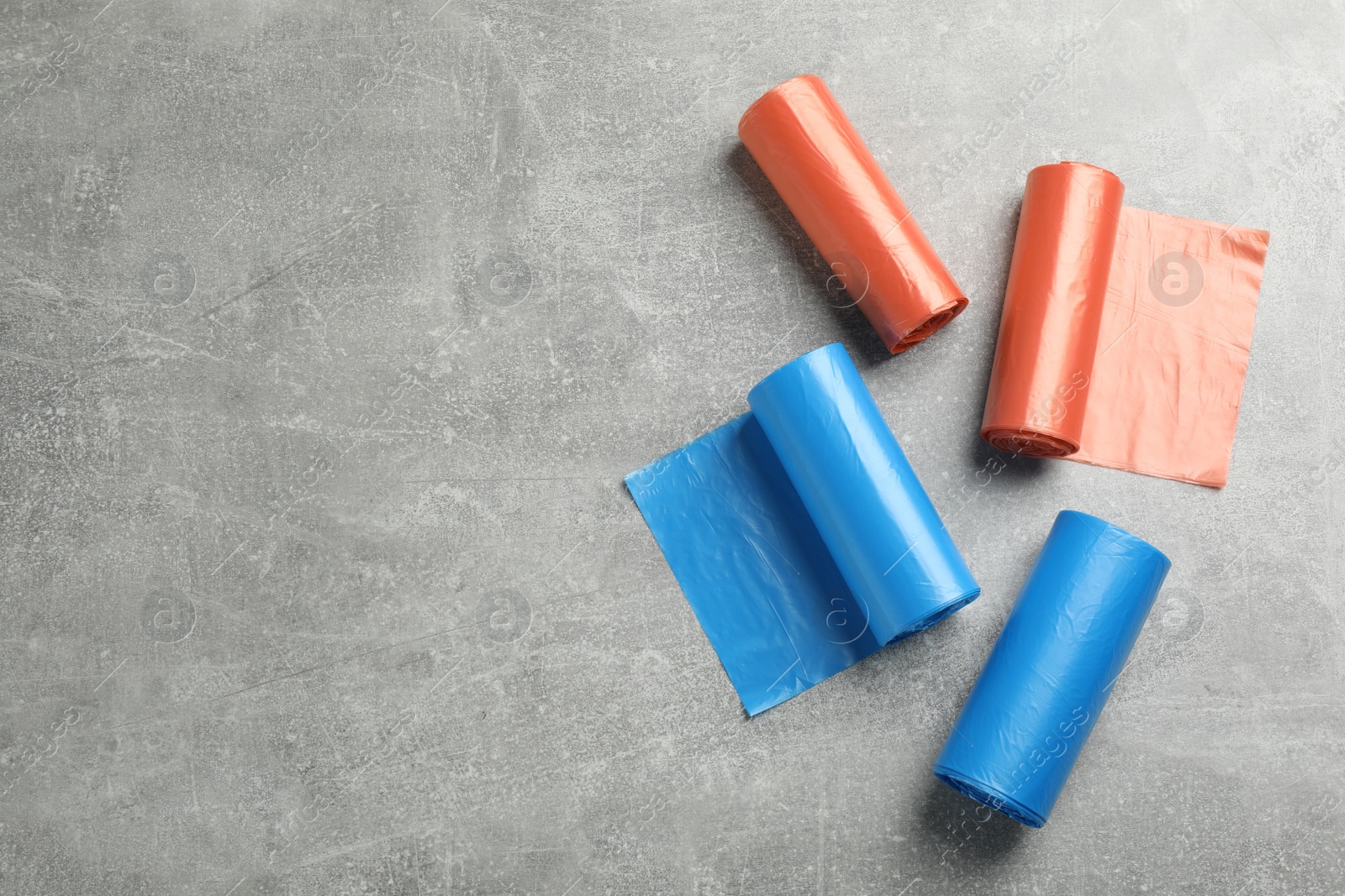 Photo of Rolls of different color garbage bags on light grey stone table, flat lay. Space for text