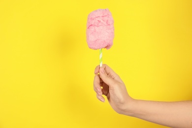 Photo of Woman holding straw with fluffy cotton candy on color background, closeup