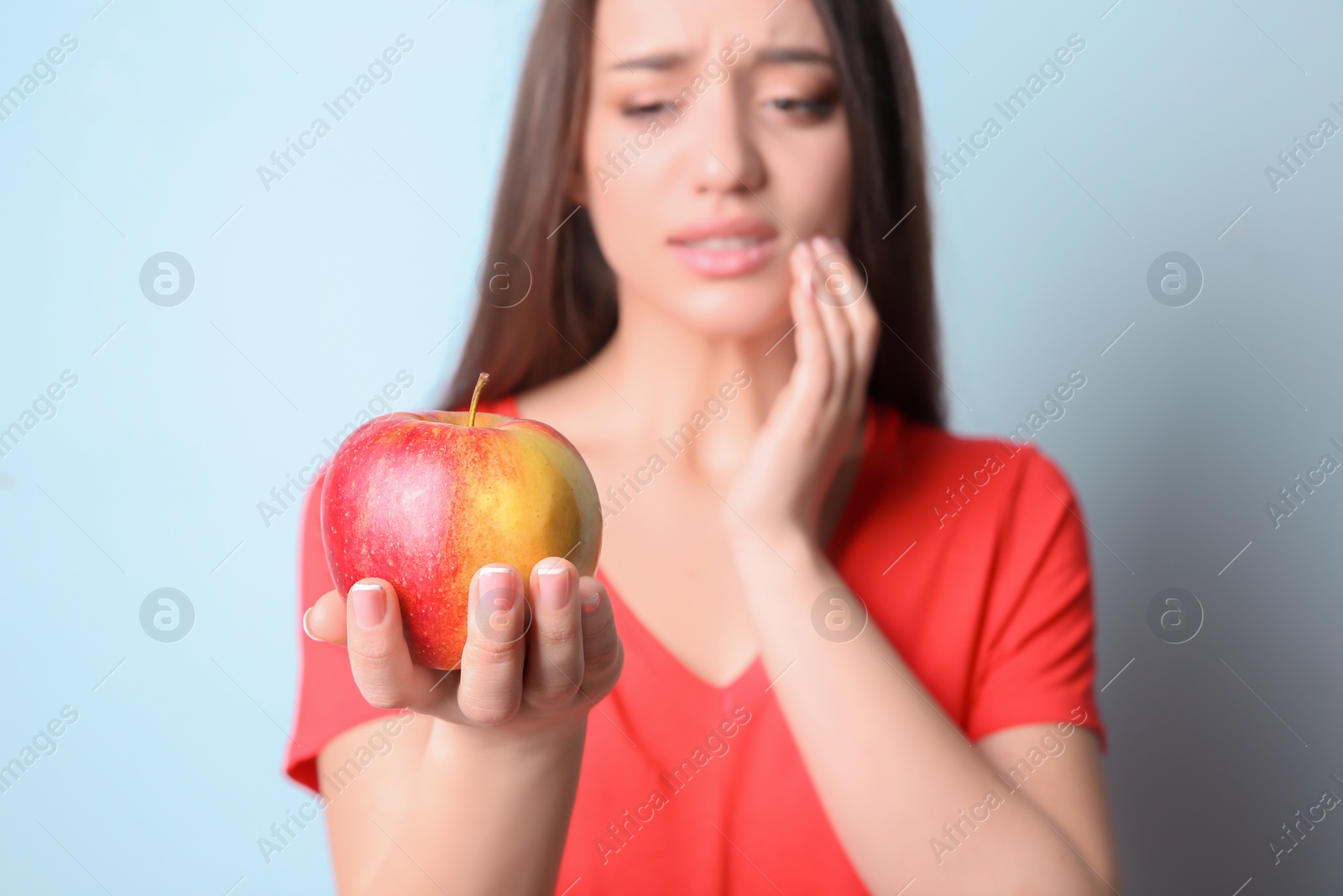 Photo of Woman with sensitive teeth holding apple on color background