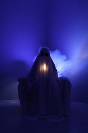 Photo of Creepy ghost. Woman covered with sheet in armchair in blue light