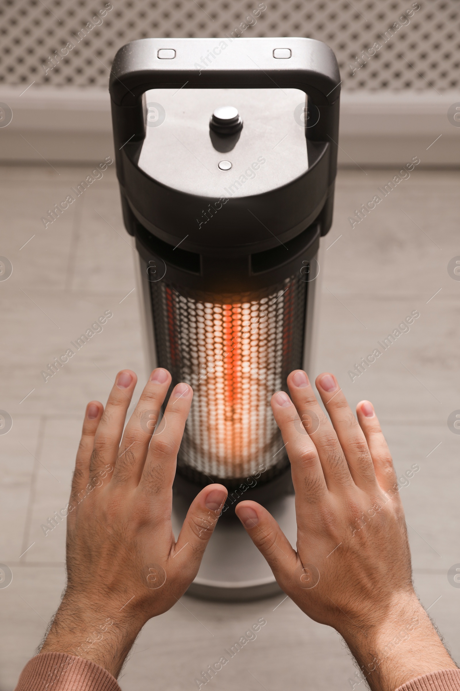 Photo of Man warming hands near modern heater indoors, closeup