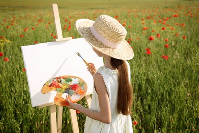 Photo of Little girl painting on easel in beautiful poppy field